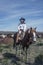 Cowboy wrangler with black hat and blue bandanna riding a paint horse is watching over the horse herd as they rest on the annual G