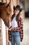 Cowgirl with a big smile feeds her horse from the hand inside the stable