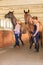 Cowgirl and jockey walking with horses in stable