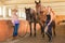 Cowgirl and jockey walking with horses in stable