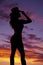 Cowgirl standing in the sunset silhouette holding hat