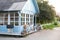 Cozy blue home with a beautiful garden in summer. Beautiful farmhouse with wicker baskets and green plants on terrace. White table