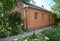 Cozy brick house with asbestos roof and red clibing roses, beautiful flower bed.