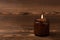 Cozy burning candle in brown glass jar on brown texture wood.