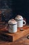 Cozy Christmas composition.Two mug with hot drinks, chocolate with whipped cream and cinnamon stick on a dark wooden background.