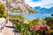 Cozy city street of Limone Sul Garda with paving stone sidewalk, blooming flowers on a metal railings, growing trees with amazing