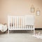Cozy classic crib in a light baby room with toys on a soft carpet and a woven basket on the corner