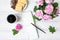 Cozy composition with cup of coffee, sketchbook and roses against white vintage wooden table. Flat lay, top view