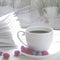 Cozy concept: a white cup of coffee stands on a white wooden table next to a white open book and colorful candy against the