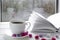 Cozy concept: a white cup of coffee stands on a white wooden table next to a white open book and colorful candy against the