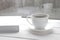 Cozy home still life: white cup of hot coffee and white opened book on windowsill against snow landscape outside