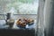 Cozy home tea party by window in bad weather. Porcelain white teapot and cup with tea, homemade berry pie on a round blue plate