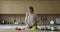 In cozy kitchen, mature female cut cucumber for vegetable salad