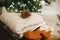 Cozy knitted sweaters and wool socks on rustic wood with pine cone on background of christmas tree lights. Pile of stylish winter