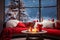 Cozy living room interior with red sofa, candles and Christmas decorations on the windowsill. Winter landscape.