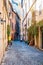 Cozy narrow ancient medieval Old Town paving stone street with green overgrown facades, small businesses, parked mopeds in Rome,