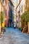 Cozy narrow ancient medieval Old Town paving stone street with green overgrown facades, small businesses, parked mopeds in Rome,