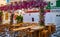 Cozy outdoor dining, cafe, restaurant, taverna in small Greek square, whitewashed chapel, vibrant pink bougainvillea in