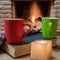 Cozy scene before fireplace with red and green mugs with tea, candle, book and wool scarf