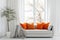 Cozy sofa with orange cushions near white wall with curtain against window