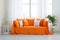 Cozy sofa with orange cushions near white wall with curtain against window