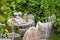 Cozy tea party at garden with book, teapot, candle, flowers, blanket. Beautiful metal lacy chairs and table.