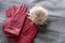 Cozy and warm winter flat lay with copy space. Dark red knitted hat with fur pompom and burgundy gloves on gray background