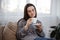 Cozy young woman drinking coffee in living room