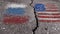 Crack, burst asphalt coating. Textured surface, selective focus. Rear grey background. The Russian and American flags