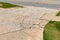 Cracked and broken aggregate concrete driveway descending into an asphalt roadway, flanked by green grassy areas, creative copy sp