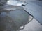 Cracked and broken asphalt pothole with water on the surface of