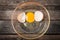 Cracked chicken egg with yolk and egg shell on dish, wooden background