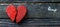 Cracked red heart symbol on dark textured wooden background for emotional concept