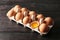 Cracked and whole chicken eggs in carton pack on dark wooden table