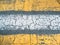 Cracked yellow and white paint lines on grey asphalt road texture, top view as grunge background or wallpaper