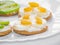 Crackers with banana and avocado slices, cream cheese, raisins and sesame seeds on a white plate. Healthy diet. Close-up