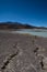 Cracks in the dry desert sand leading the eye to the green Laguna Honda