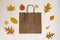 Craft brown shopping bag surrounded by yellow and orange fallen autumn leaves, the concept of autumn discounts