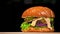 Craft burger is cooking on black background. Consist: sauce salsa, lettuce, red onion, pickle, cheese, chilli green