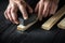 The craftsman cleans the wood plank with an abrasive tool. Builder hands close up. Renovation or construction idea