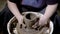 Craftsman is producing ceramic pot in a rotating wheel-head, removing excess clay by hands to refine shape in a pottery