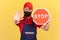 Craftsman in uniform and hygienic face mask showing stop gesture and holding red stop road sign, prohibitions and restrictions
