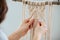 Craftswoman weving ropes, creating a macrame banner. from behind
