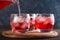 Cranberry juice pouring into glasses with berries and ice cube on the wooden cutting board.