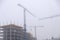 Crane on the background of under construction skyscrapers in a fog on an abandoned