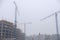 Crane on the background of under construction skyscrapers in a fog on an abandoned