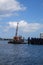 A crane on calm water seen on a barge by a dock on a sunny day with some white clouds