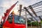 A crane driver is steering a crane to lift a roof or PU foam roof sheet onto a steel roof structure at a construction site.