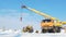 Crane holds cable for high voltage line among snow under blue sky