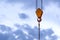 Crane hook with hanging cable against the blue sky and clouds